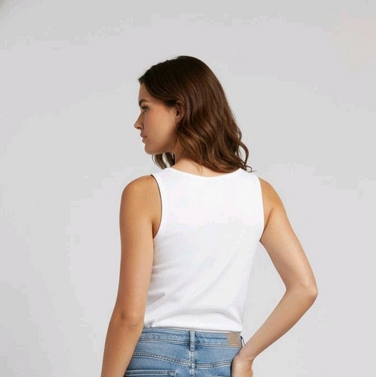 Woman wearing a white tank top and light blue jeans on a plain background